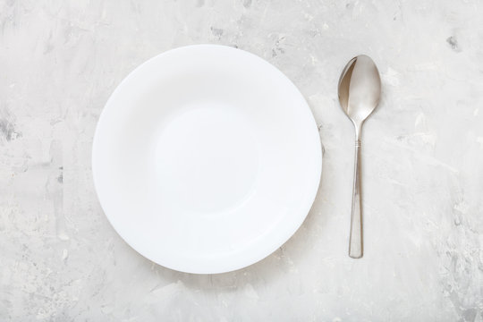 top view of white deep plate and spoon on concrete