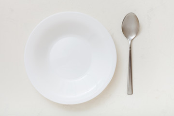 top view of white deep plate and spoon on plaster
