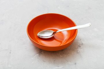 one orange bowl with spoon on gray concrete