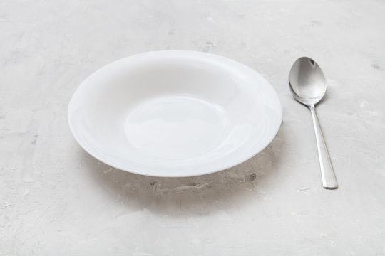 white deep plate and metal spoon on gray concrete