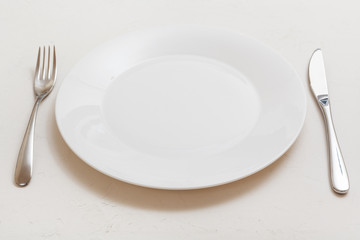 white plate with knife, spoon on white plaster