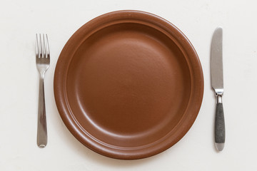 top view of brown plate with knife, spoon on white