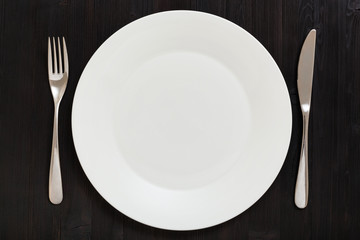 top view of white plate with knife, spoon on dark