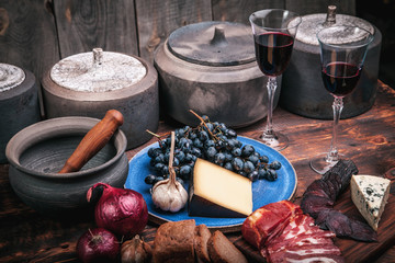 Meat and cheese appetizers selection on a rough old wood background with grapes, two glasses of wine and pottery