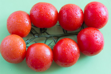  red tomatoes with green leaves. Top view. Green background.