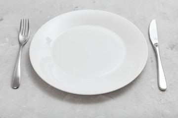 white plate with knife, spoon on gray concrete