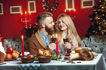 Beautiful couple in a decorated festive interior with a Christmas tree drinking wine. A romantic dinner for thanksgiving with fried chicken and candles