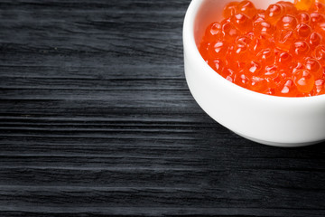 Red caviar in a cup with salt on a wooden table