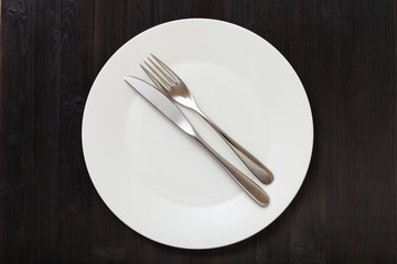 top view of white plate with flatware on dark