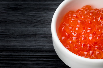 Red caviar in a cup with salt on a wooden table