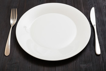 white plate with knife, spoon on dark brown table