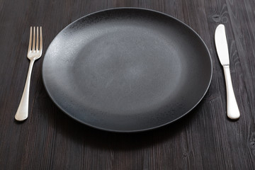 black plate with knife, spoon on dark brown table