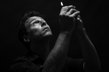 Man pray with a lighter in his hand. Low key , black and white portrait.