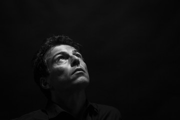 Isolated thinking man face looking up. Low key , black and white portrait.