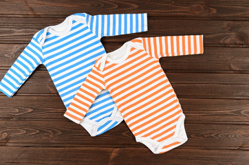 Two striped baby bodysuits on wooden background