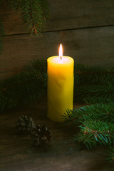 Fototapeta na wymiar Christmas lighted candle with christmas tree and cones on wooden background