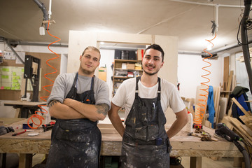two carpenters look at the camera and smile. inside the workshop