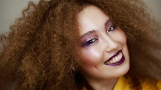 Beautiful Asian girl with bright makeup and curly hair smiling happily