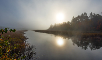 Fototapeta na wymiar Morning mist and fog rises from warm water into autumn October air on Corry lake, Ontario, Canada.