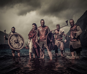 A group of armed Vikings standing on river shore