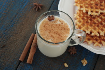 milk with cinnamon in a transparent mug, waffles, cakes, tied with Christmas ribbon, anise on blue wooden background