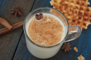 milk with cinnamon in a transparent mug, waffles, cakes, tied with Christmas ribbon, anise on blue wooden background