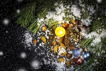 Pine branches, candle, Christmas tree decorations, nuts, the pine cone in snow on a black...