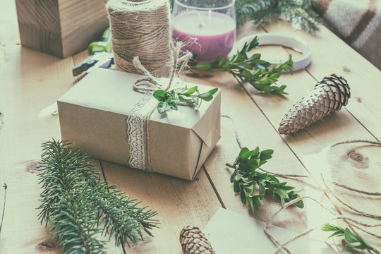 Wrapping eco Christmas packages with brown paper, string and natural branches and decor elements on wooden table
