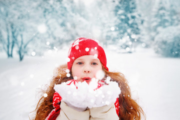 Little girl blows snow with mittens, on a snowflakes bokeh backg