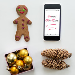 Flat view of mobile phone among cute Happy new year decoration, cones, box of glass balls, ginger man. New year concept, high angle