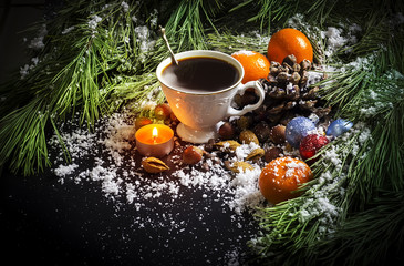 White vintage cup with hot coffee, nuts, tangerines, a candle, pine branches on a black background