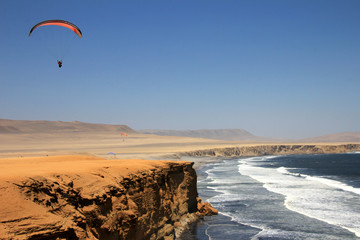 Paraglider soaring over the cliffs at oceanfront of Paracas Peru