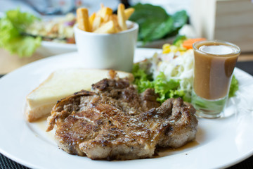Pork chop steak with french fries, breads and salads on the dish