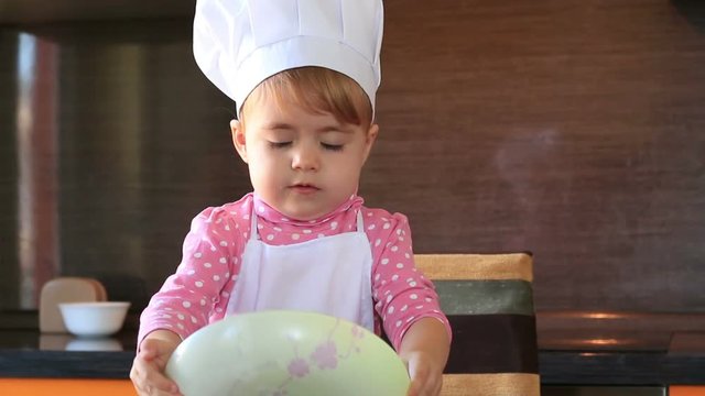 little cute girl in chef suit playing with the dishes in the kitchen