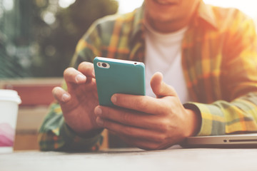 Young man with smartphone in hand sitting in street cafe, texting with friends