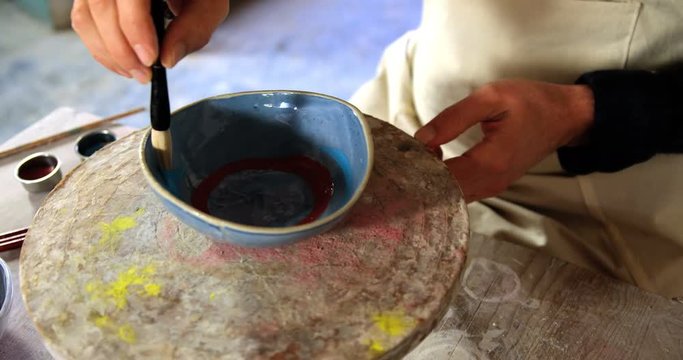 Mid-section of male potter painting on bowl