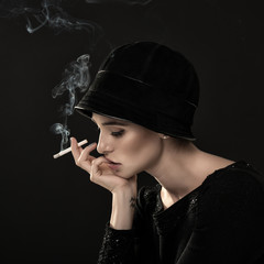 Obraz premium Young fashion woman smoking cigarette in hat and black drees ove