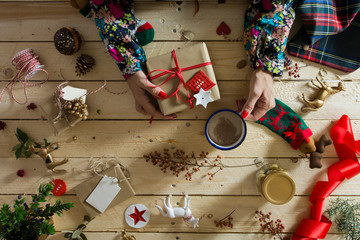 Woman decorating a Christmas present, surrounded by festive deco