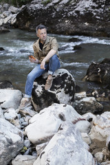 Outdoor male portrait. Handsome man sitting on rocks near mounta