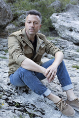 Outdoor male portrait. Handsome middle-aged man sitting on rocks