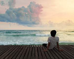 Lonely Man sitting in a wooden dock pier in sea beach with twilight sky in sunset time and think concentrate