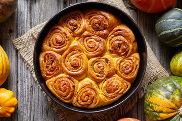 Cinnamon pumpkin dough bun rolls spicy traditional Danish baked vegan sweet autumn cake holiday dessert swirl bread pastry food with raw pumpkins on vintage wooden table background.