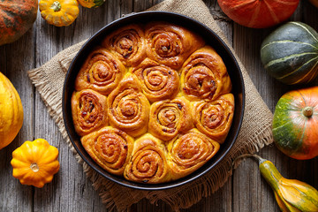 Cinnamon pumpkin dough bun rolls spicy traditional Danish baked vegan sweet autumn treat cake holiday dessert swirl bread pastry food with raw pumpkins on vintage wooden table background.