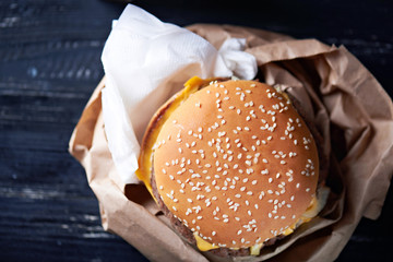 Unhealthy cheeseburger in the paper container with paper napkins on a dark wooden background. Close up