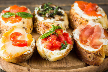 Various types of tapas. Italian tasty tomato, mushrooms, prosciutto, ham, salmon and cheese bruschetta. Antipasti with vegetables, herbs and oil on grilled ciabatta and baguette.