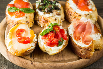 Various types of tapas. Italian tasty tomato, mushrooms, prosciutto, ham, salmon and cheese bruschetta. Antipasti with vegetables, herbs and oil on grilled ciabatta and baguette.
