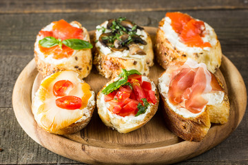 Various types of tapas. Italian tasty tomato, mushrooms, prosciutto, ham, salmon and cheese bruschetta. Antipasti with vegetables, herbs and oil on grilled ciabatta and baguette.