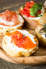 Various types of tapas. Italian tasty tomato, mushrooms, prosciutto, ham, salmon and cheese bruschetta. Antipasti with vegetables, herbs and oil on grilled ciabatta and baguette.