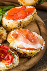 Various types of tapas. Italian tasty tomato, mushrooms, prosciutto, ham, salmon and cheese bruschetta. Antipasti with vegetables, herbs and oil on grilled ciabatta and baguette.