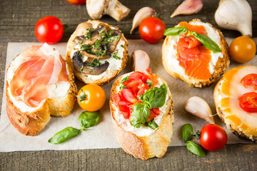 Various types of tapas. Italian tasty tomato, mushrooms, prosciutto, ham, salmon and cheese bruschetta. Antipasti with vegetables, herbs and oil on grilled ciabatta and baguette.